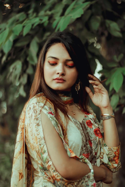 a woman standing in front of a tree, an album cover, by Riza Abbasi, pexels contest winner, beautiful young himalayan woman, red and green tones, wearing an elegant outfit, floral