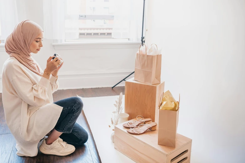 a woman sitting on the floor looking at her cell phone, by Eden Box, presenting wares, sitting in an empty white room, sustainable materials, background image