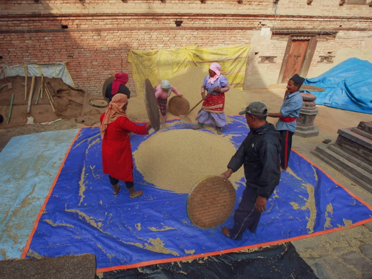 a group of people standing on top of a blue tarp, rice, churning, thumbnail, circle pit