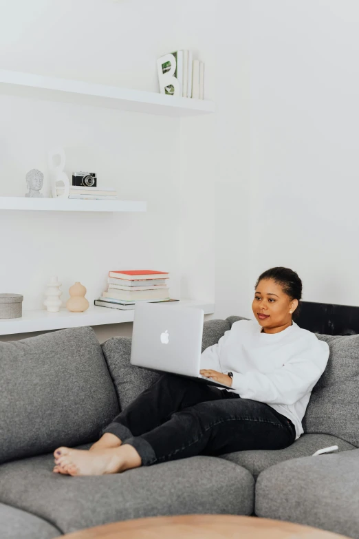 a woman sitting on a couch using a laptop, by Dulah Marie Evans, sitting in a lounge, black female, wearing a white button up shirt, in a white room