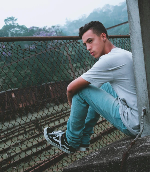 a man sitting on a ledge in front of a fence, pexels contest winner, young teen, portrait shot 8 k, ariel perez, high soles