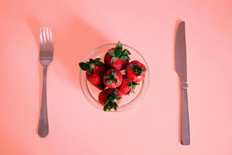 a strawberry on top of a plate next to a fork and knife