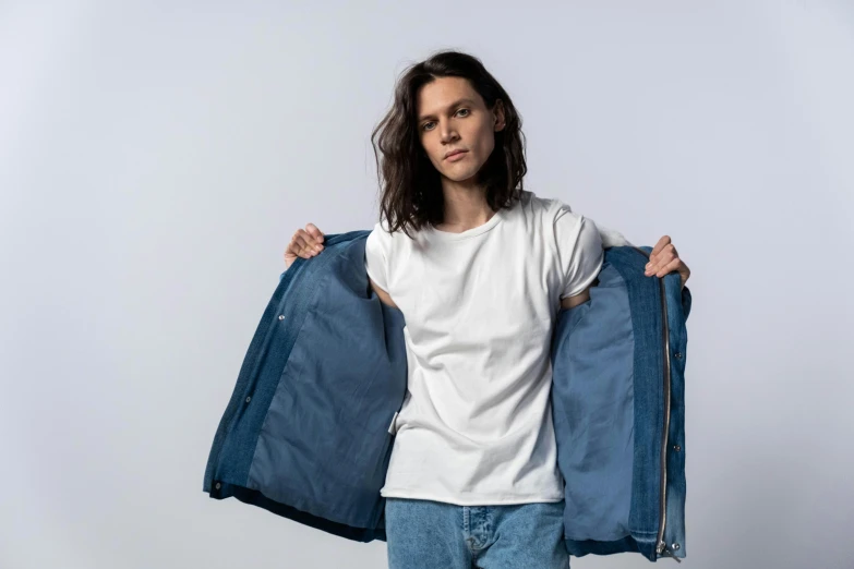 a man wearing a white t - shirt and blue jacket standing with his hands on his back