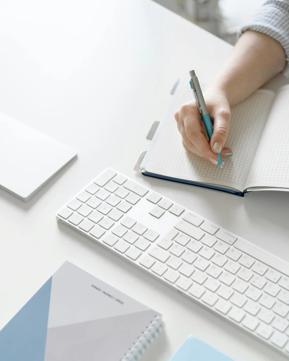 a person sitting at a desk writing on a piece of paper, a computer rendering, pexels contest winner, white and pale blue, keyboard, sustainable materials, minimal palette