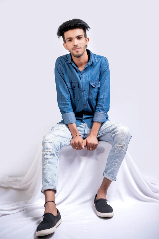 a man sitting on top of a white sheet, inspired by Saurabh Jethani, pexels contest winner, wearing double denim, studio photoshot, thin young male, ( ( ( wearing jeans ) ) )