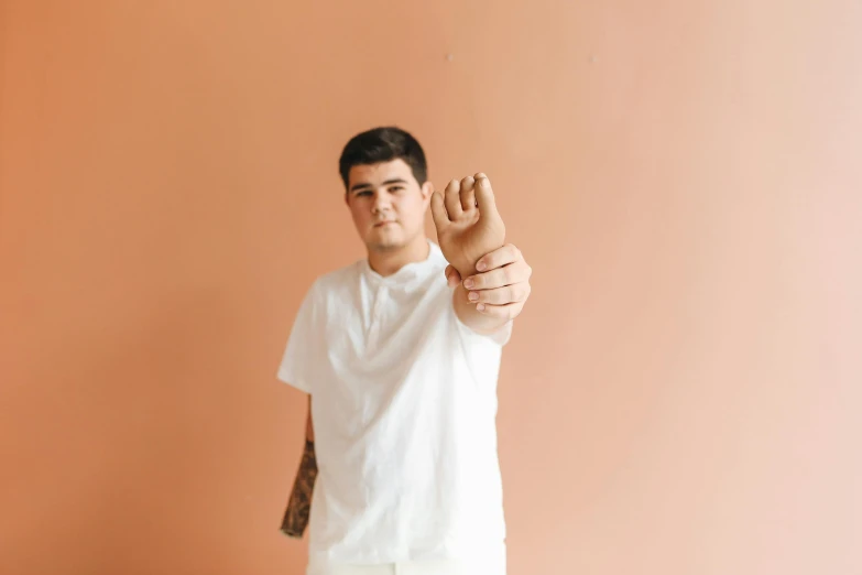 a man standing in front of a pink wall, an album cover, by Jessie Alexandra Dick, pexels contest winner, realism, white bandages on fists, wearing an orange t shirt, slightly overweight, asher duran