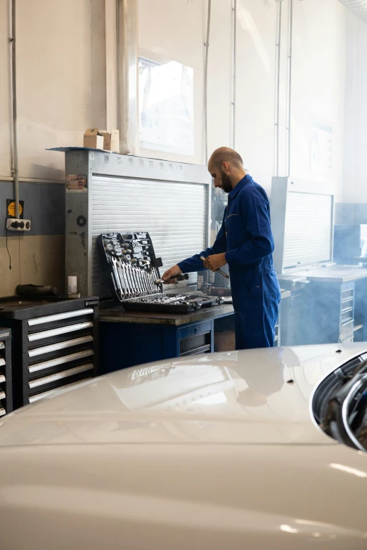 a man working on a car in a garage, a photo, arbeitsrat für kunst, aftermarket parts, diagnostics, blue, plating