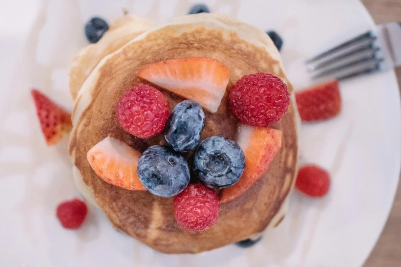 fruit and pancakes on a white plate with a fork