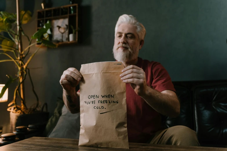 a man sitting on a couch holding a paper bag, pexels contest winner, on kitchen table, hidden message, overalls and a white beard, avatar image