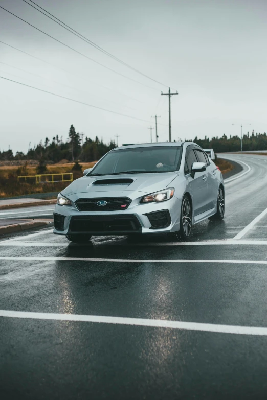 the front view of a white subarunt driving down a wet street