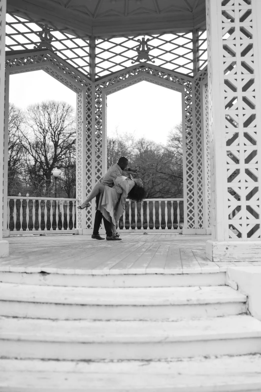 a black and white photo of a couple kissing under a gazebo, flickr, arabesque, in london, walking over you, filmstill, riyahd cassiem