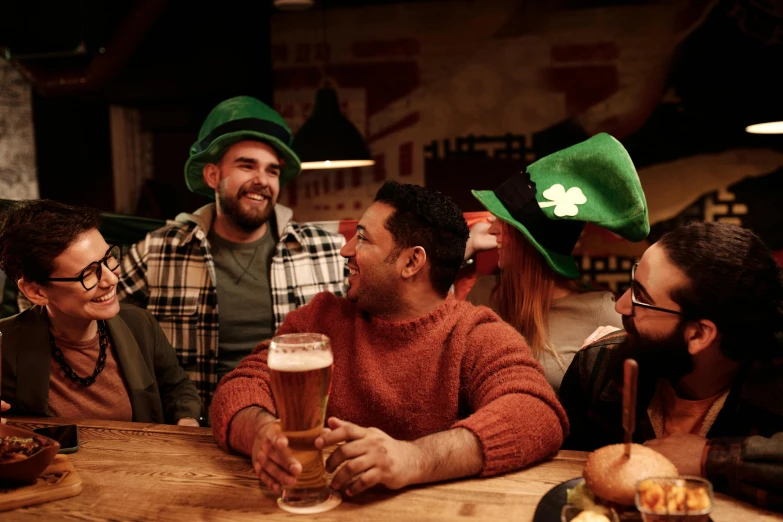 a group of people sitting around a wooden table, green hat, beer glasses, four leaf clover, 🚿🗝📝