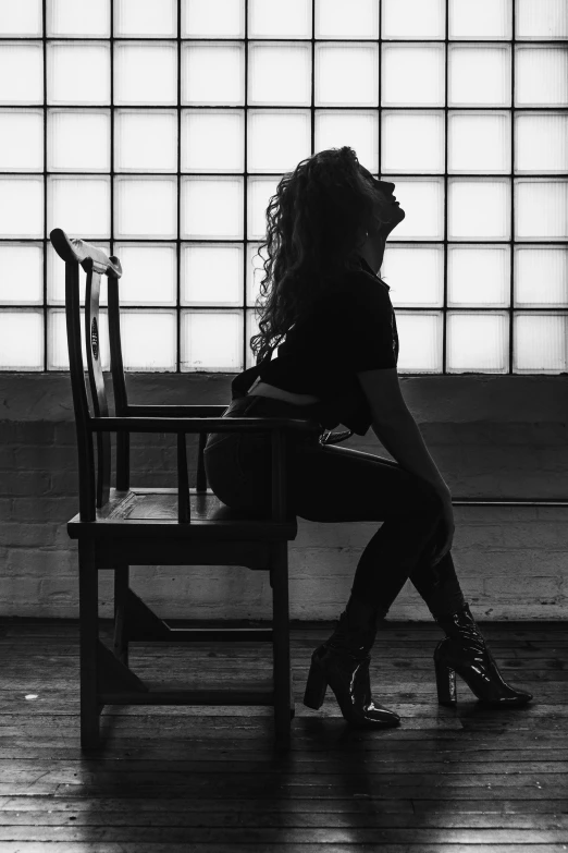 a woman sitting on a chair in front of a window, a black and white photo, inspired by Elsa Bleda, unsplash, dominatrix, beyonce, silhouette!!!, sza