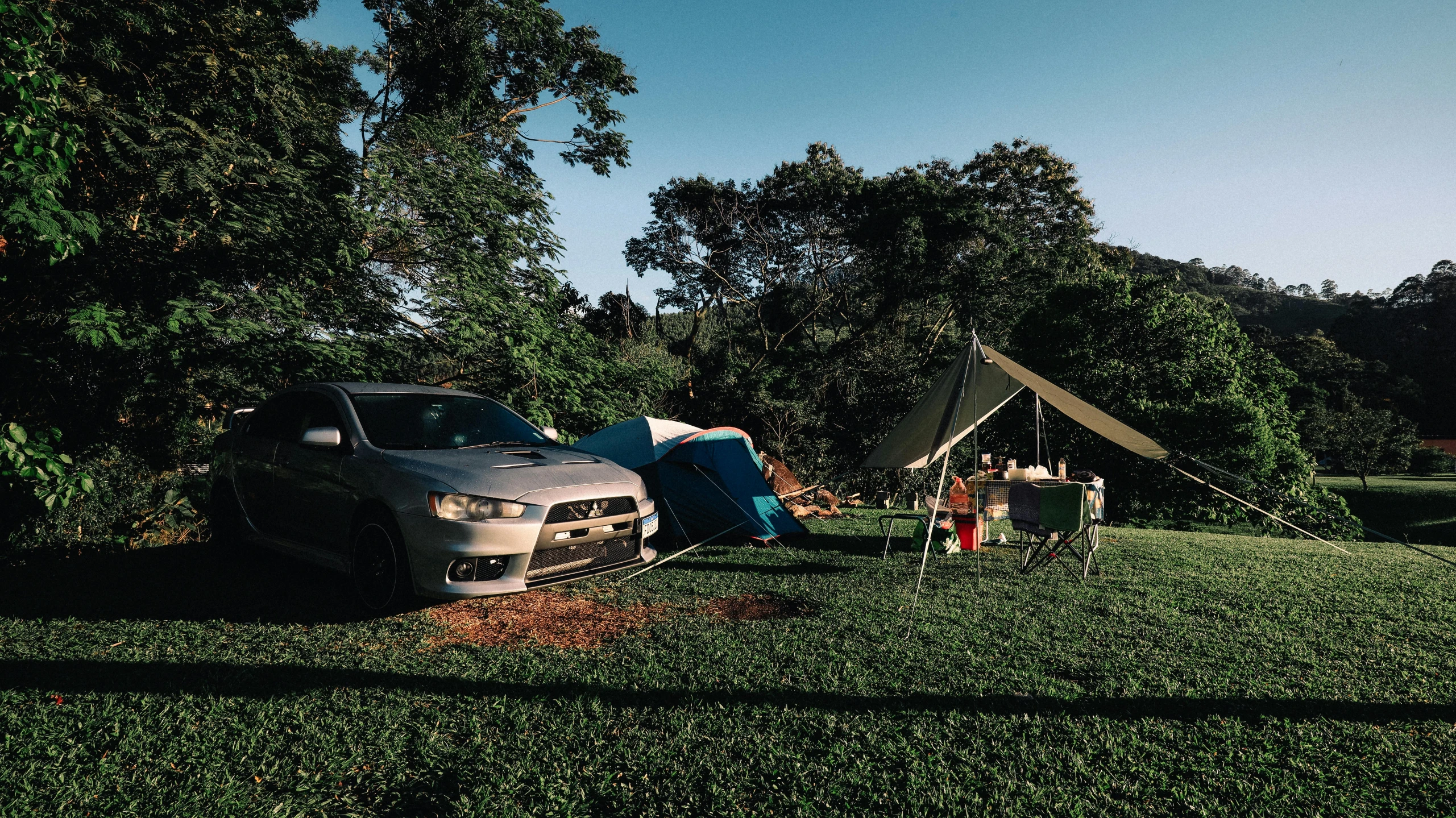 a car parked next to a tent on top of a lush green field, party in jungles, bulli, encampment, set photo