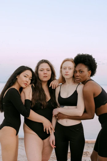 a group of women standing next to each other on a beach, inspired by Vanessa Beecroft, unsplash, mixed-race woman, black velvet, pale glowing skin, standing on rooftop