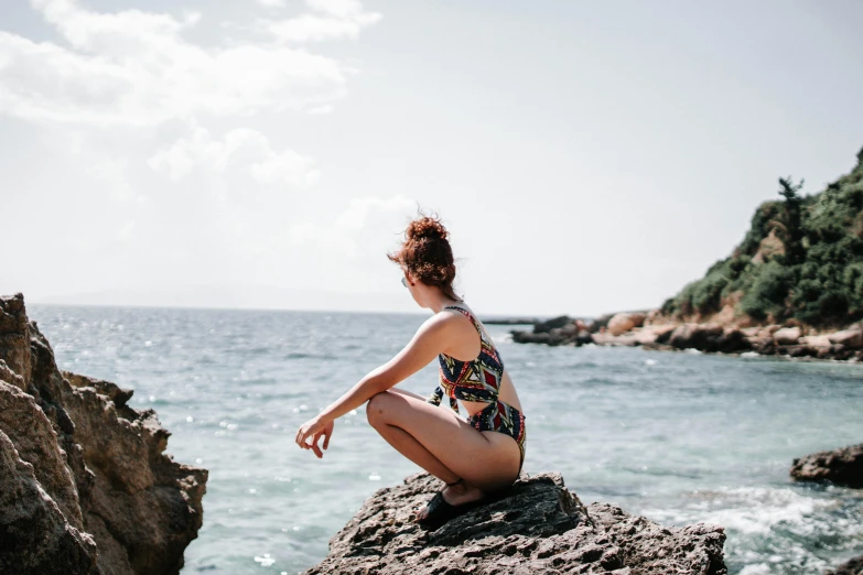 a woman sitting on top of a rock next to the ocean, monokini, profile image