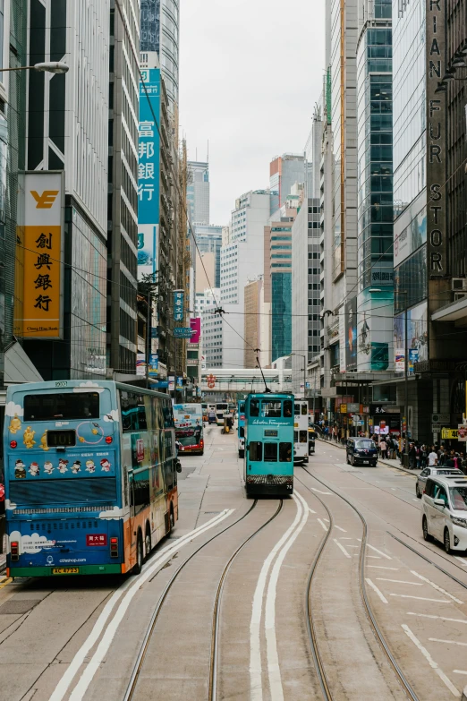 a couple of buses driving down a street next to tall buildings, by Patrick Ching, trending on unsplash, city like hong kong, trams, square, ancient city streets behind her