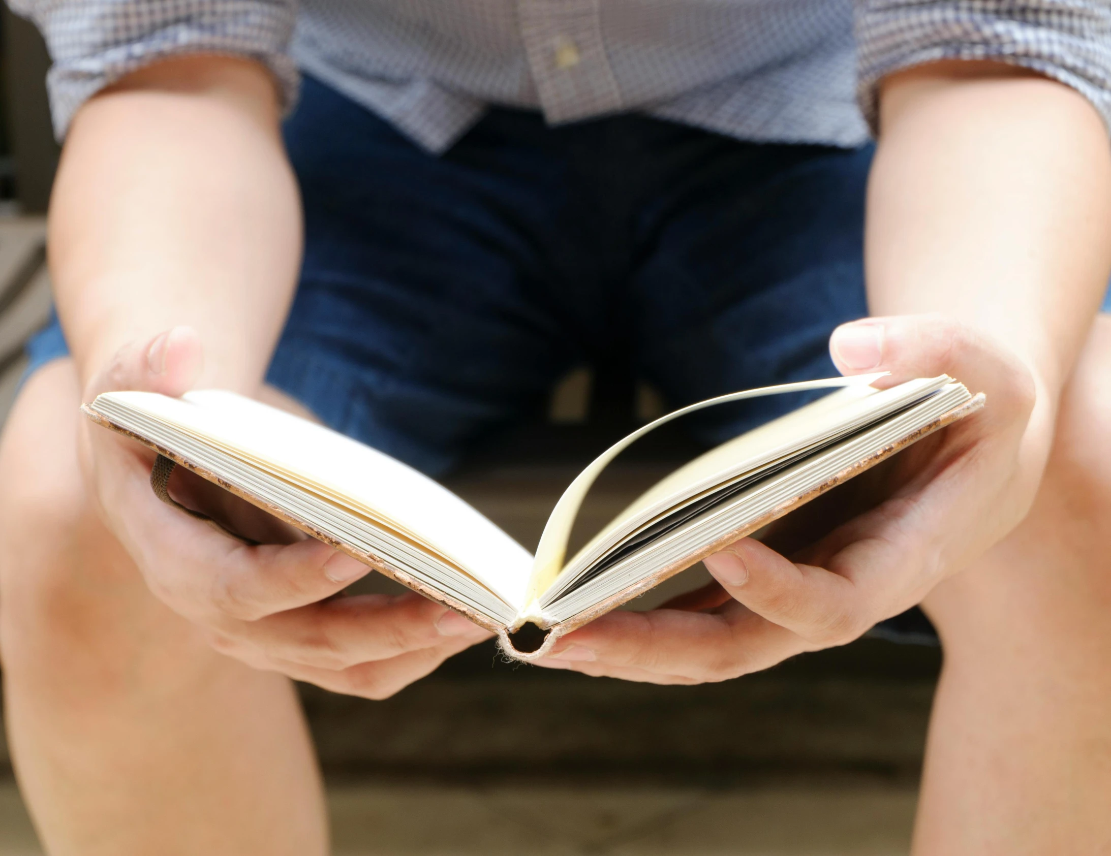 a person sitting on a bench reading a book, by Carey Morris, pexels, he is holding a large book, coherent hands, plain background, from reading to playing games