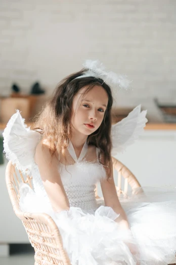 a little girl in a white dress sitting on a wicker chair, by Marie Angel, pexels contest winner, renaissance, with real wings, gif, frown fashion model, on a white table