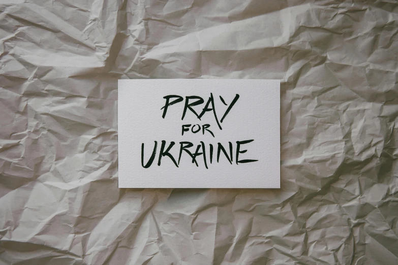 a piece of paper with the words pray for ukraine written on it, an album cover, canva, alternative, background image, unknown artist