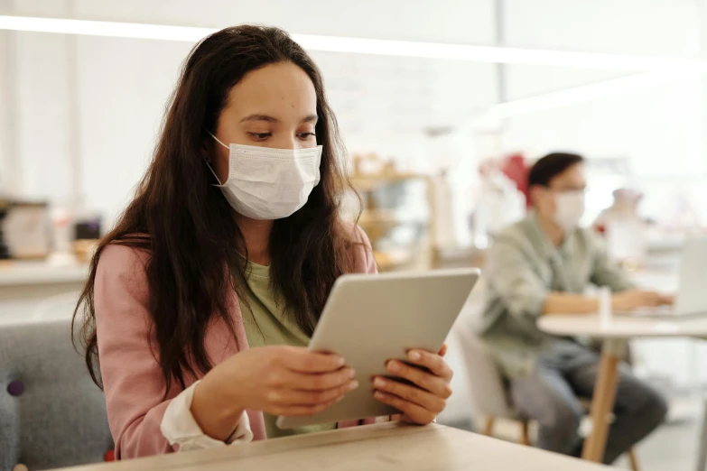 a woman sitting at a table using a tablet computer, a picture, trending on pexels, happening, people are wearing masks, person in foreground, disease, thumbnail