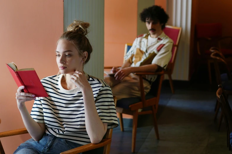 a woman sitting in a chair reading a book, inspired by Balthus, pexels, two buddies sitting in a room, wearing stripe shirt, julia garner, waiting room