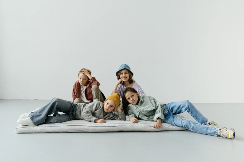 a group of people laying on top of a mattress, by Nina Hamnett, trending on pexels, kid, baggy clothing and hat, grey backdrop, 1505