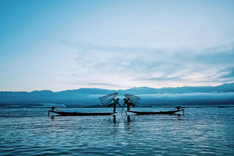 a couple of people standing on top of a boat, by Jessie Algie, unsplash contest winner, hurufiyya, myanmar, blue hues, fishes swimming, in the early morning