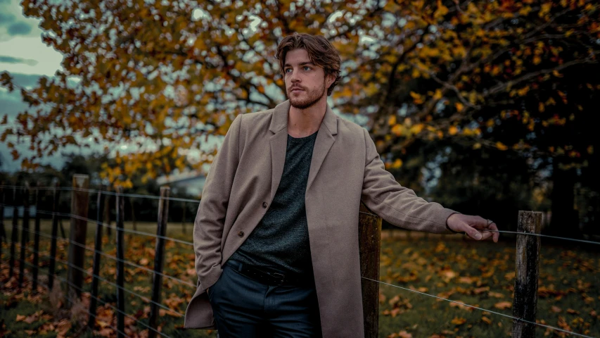 a man wearing a coat standing near a fence