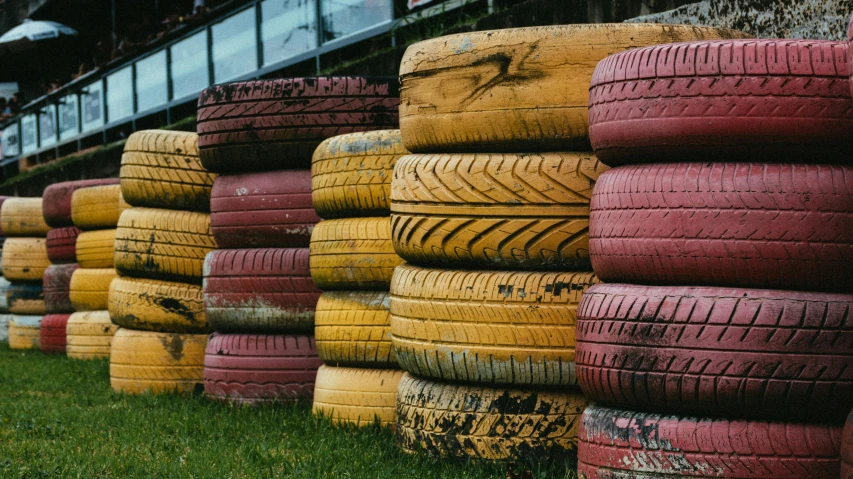 a row of tires sitting on top of a lush green field, pink and yellow, industrial colours, brown, formula 1 garage