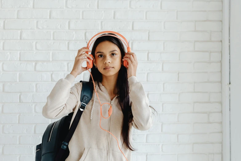 a woman with headphones standing in front of a brick wall, trending on pexels, in school hallway, indian girl with brown skin, greta thunberg, on a pale background