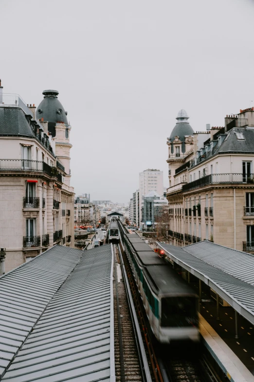 a train traveling down train tracks next to tall buildings, trending on unsplash, paris school, square, roofs, low quality photo, french village exterior