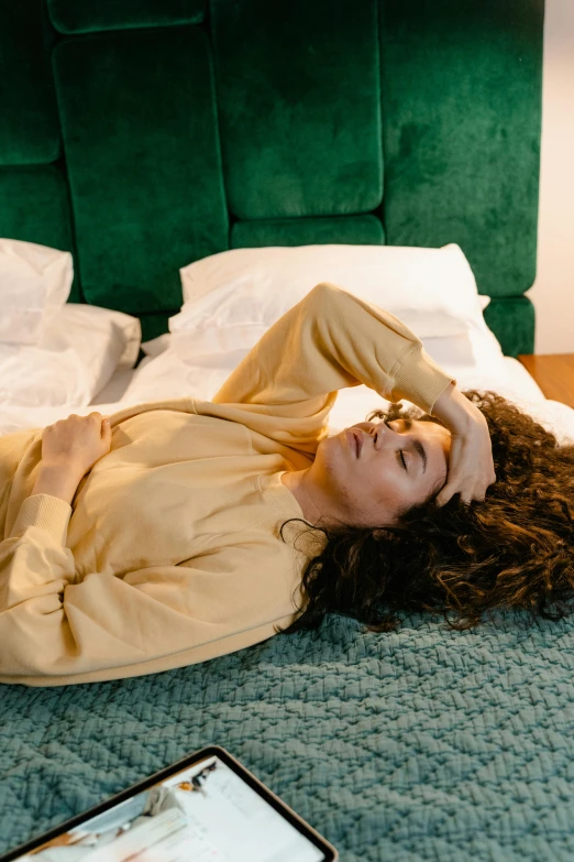 a woman laying on top of a bed next to a laptop, inspired by Elsa Bleda, trending on pexels, renaissance, curls on top of his head, wearing a green sweater, non binary model, hotel room