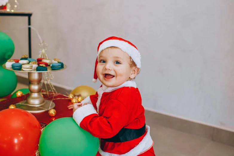 baby dressed as santa clause holding christmas balloons