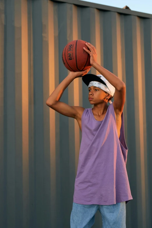 a man holding a basketball over his head, by Greg Spalenka, dribble contest winner, portrait willow smith, wearing a purple cap, evening time, wearing a muscle tee shirt