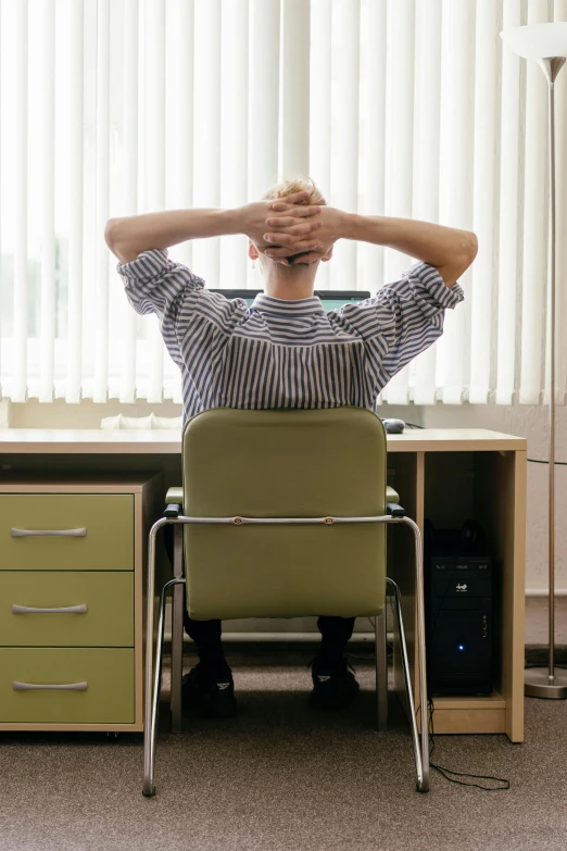 a man sitting at a desk with his hands behind his head, by Paul Bird, pexels, with his back turned, office furniture, dressed in a worn, healthcare