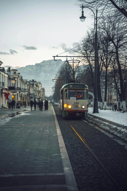 a bus driving down a street next to tall buildings, unsplash contest winner, socialist realism, light snow, ground level view of soviet town, tram, hill