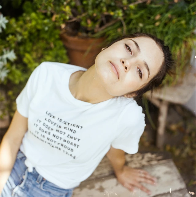 a woman sitting on top of a wooden bench, a portrait, by Nina Hamnett, unsplash, happening, printed on a cream linen t-shirt, dafne keen, love is the most relevant theme, with soft bushes