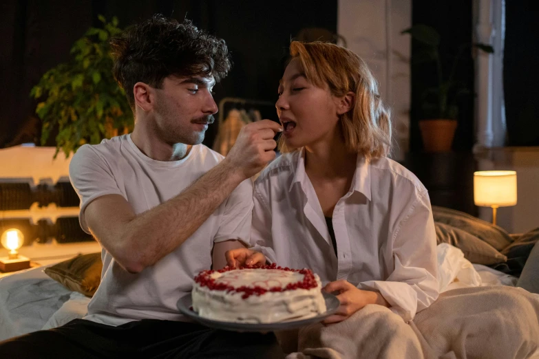 a man and a woman sitting on a couch eating cake, by Adam Marczyński, pexels contest winner, asian female, whipped cream on top, bisexual lighting, with a long