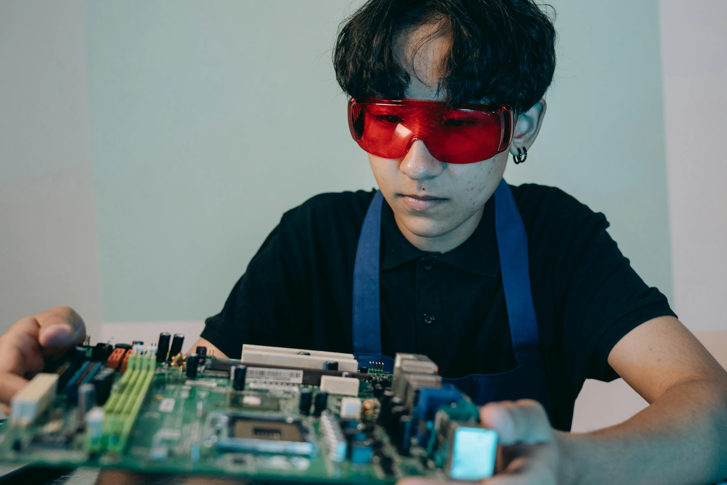 a close up of a person holding a circuit board, wearing red tainted glasses, high school, sitting at a computer, mining