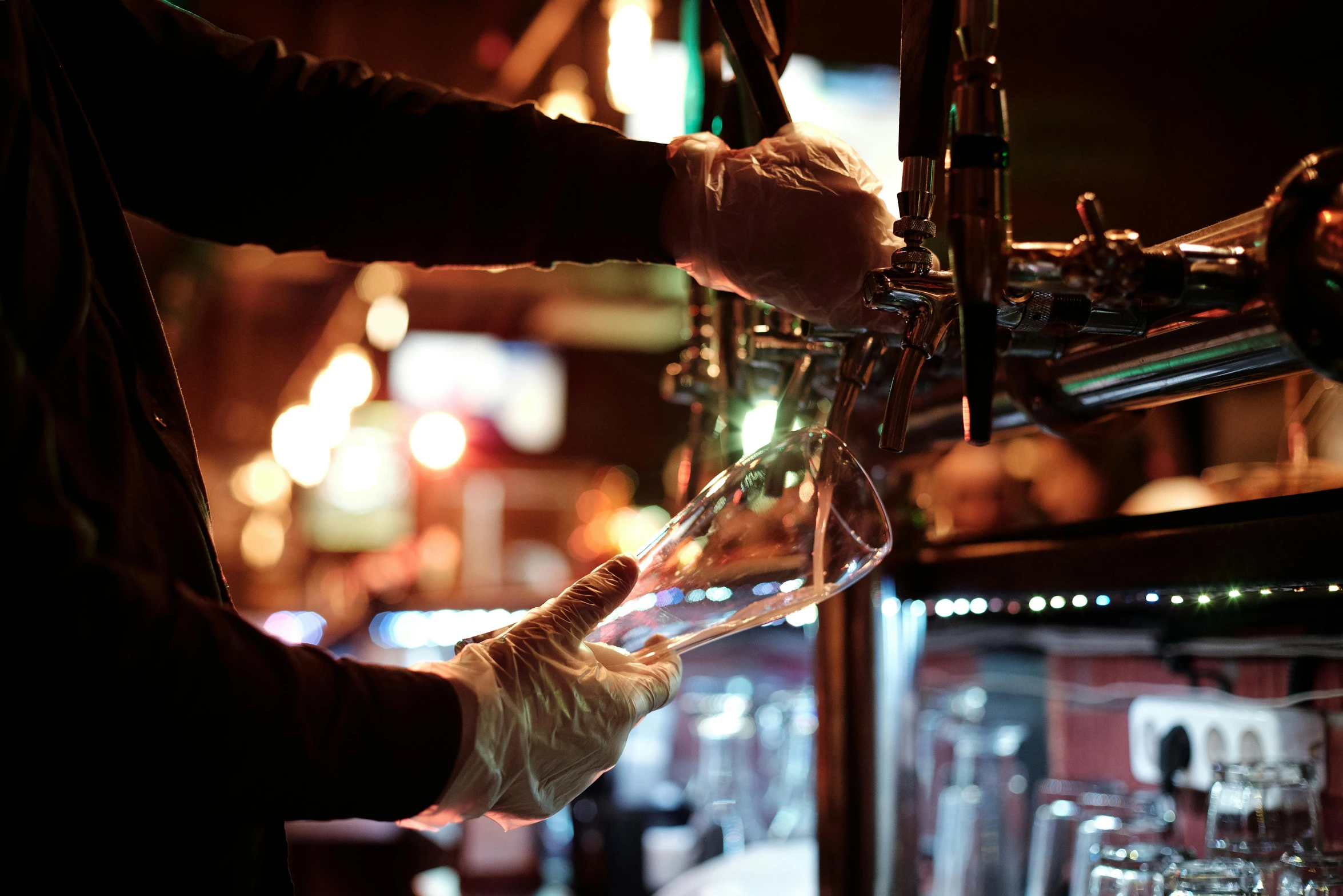 a man that is standing in front of a bar, inside a beer glass, pouring, during the night, levers