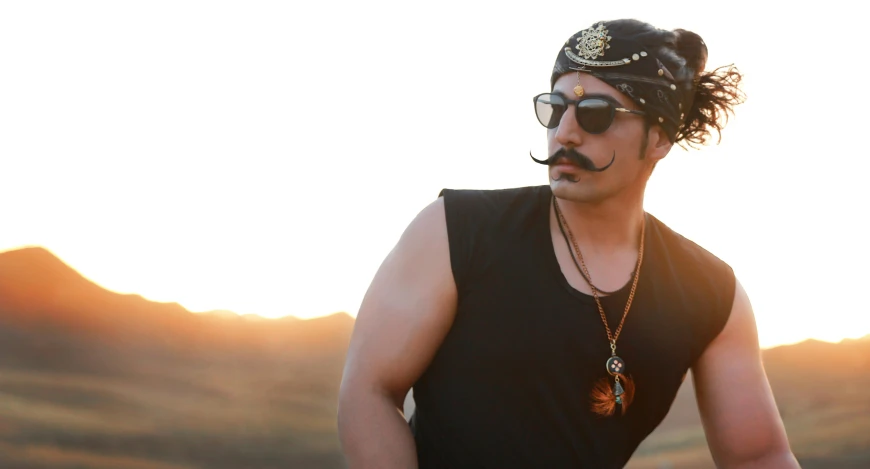 a young man with sunglasses on and mustache in a field