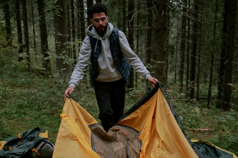 a man standing next to a tent in the woods, by Emma Andijewska, hurufiyya, yellow carpeted, sleeping bag, multi-part, brown