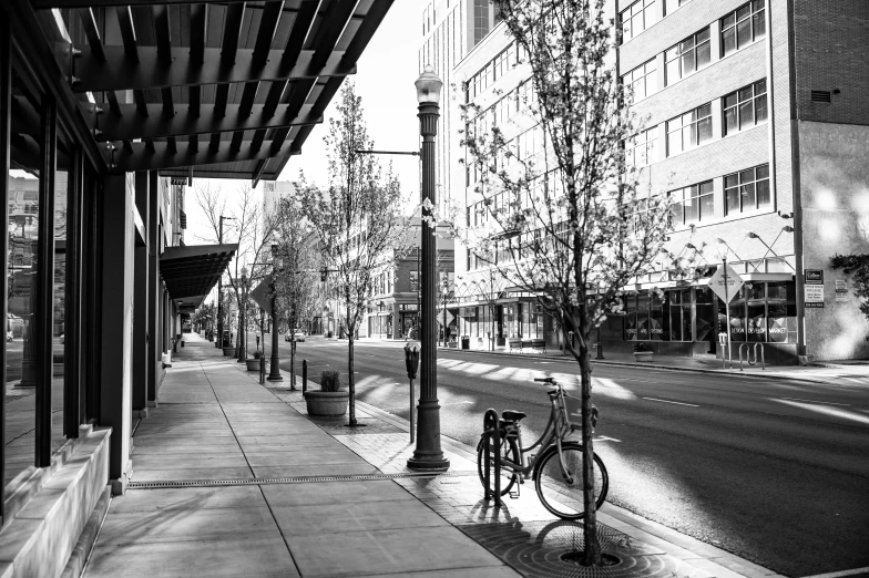 a black and white photo of a bike parked on a sidewalk, by Randall Schmit, springtime morning, downtown, with a long, idaho