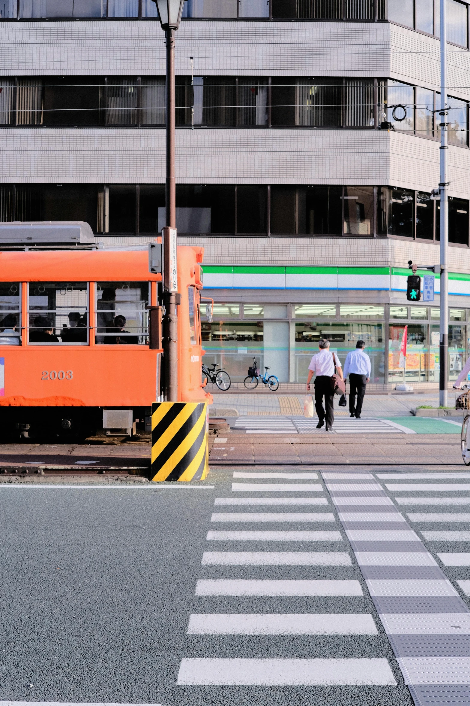 an orange trolley going down a track next to a pedestrian crosswalk