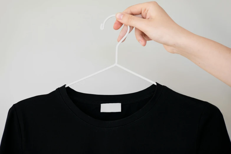 the left hand of a person holding a t - shirt on a hanger