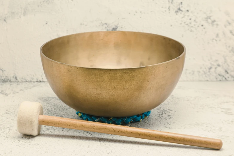 a golden singing bowl with a wooden mallet next to it, unsplash, minimalism, grey, bowl, blond, bronze