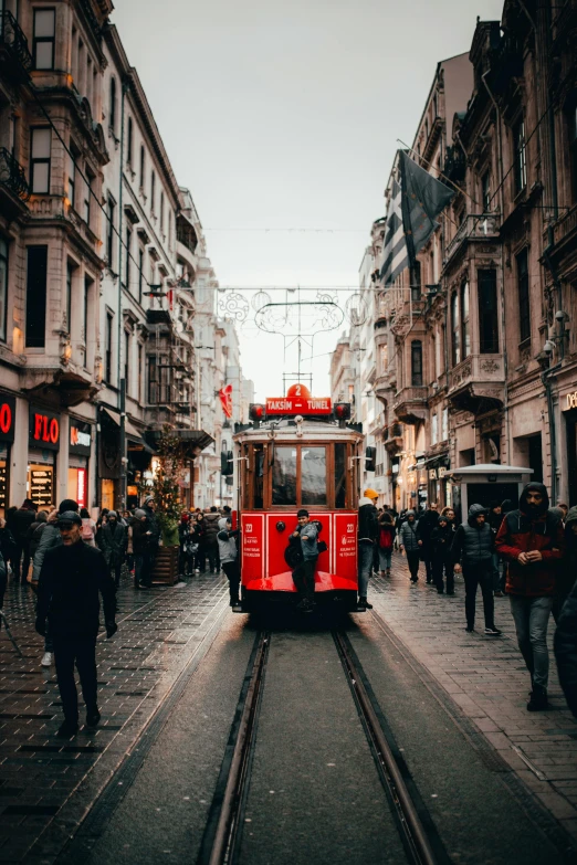 a red trolley traveling down a street next to tall buildings, pexels contest winner, ottoman empire era, busy streets filled with people, gif, square