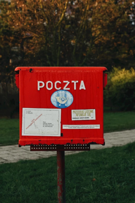 red mailbox in the middle of the park, with a sign