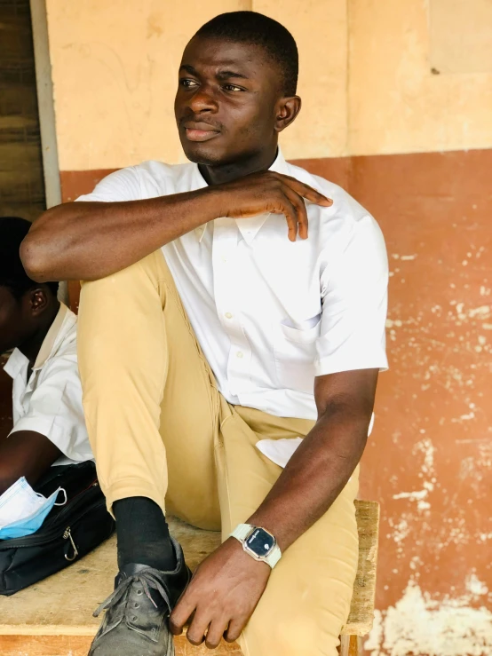 a man sitting on the steps of a building, by Chinwe Chukwuogo-Roy, trending on unsplash, wear's beige shirt, wearing school uniform, low quality photo, sitting on a stool